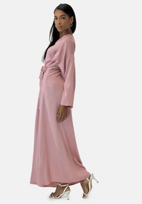 Lang, blød lyserød kjole med bælte i taljen, vide ærmer og en flydende silhuet, kombineret med hvide hæle.