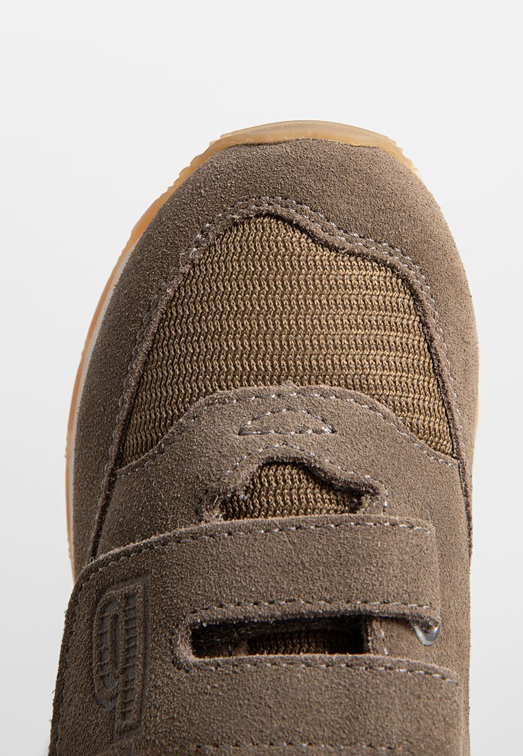 Braune Wildleder- und Mesh-Sneaker-Spitze mit einem Klettverschluss und detaillierter Steppnaht auf einem weißen Hintergrund.