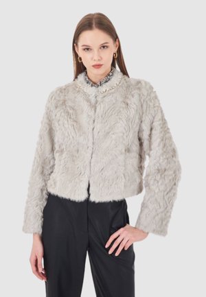 Giacca in pelliccia sintetica tagliata di grigio chiaro, con una texture morbida, collo rotondo e maniche lunghe. Abbinata a pantaloni neri a vita alta.