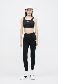 Black athletic crop top and high-waisted leggings, both made of stretchy material. White sneakers with black accents complete the outfit.