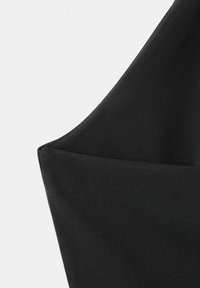 Črno blago z ostrim, kotnim pregibom, ki tvori geometrijsko obliko na enostavni beli podlagi.