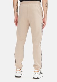 Jogging in cotone beige con una vestibilità slim, caratterizzati da una striscia laterale a motivi, vita elastica e polsini a coste. Abbinati a sneakers bianche.