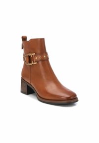 Bota de cuero marrón hasta el tobillo con tacón cuadrado, que presenta un hebilla decorativa y tachuelas en la correa. Recortada para una silueta aerodinámica.