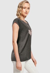 Mørkegrå strikket t-shirt med korte ærmer, der har et pink hjerte grafik på fronten. Glat tekstur, afslappet pasform og v-hals design.