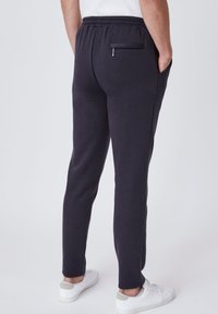 Donkergrijze sweatpants met een slim fit, elastische tailleband en zijzakken. Voorzien van een achterzak met rits. Gecombineerd met witte sneakers.