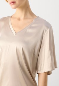 Beige sateng V-hals topp med korte ermer, med et flytende design og myk tekstur. Fremhever en subtil glans og minimal detaljering.