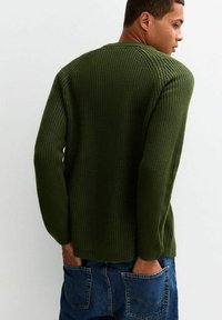 Suéter de punto verde oscuro con un patrón texturizado, cuello redondo y hombros caídos, combinado con jeans de mezclilla azul.