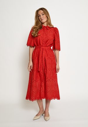 Vestito rosso al ginocchio con colletto, maniche corte a sbuffo e cintura in vita. Presenta motivi traforati e bordi smerlati.