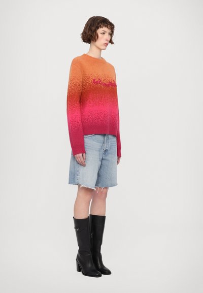 Sweter dzianinowy z gradientowym wzorem przechodzącym od pomarańczowego do różowego, z długimi rękawami. W zestawieniu z dżinsowymi szortami i czarnymi kozakami na obcasie do kolan.
