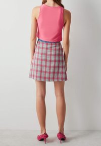 Top rosa sin mangas combinado con una minifalda de cuadros en tonos de rosa, blanco y verde. Zapatos de tacón rosas con detalles de volantes completan el conjunto.