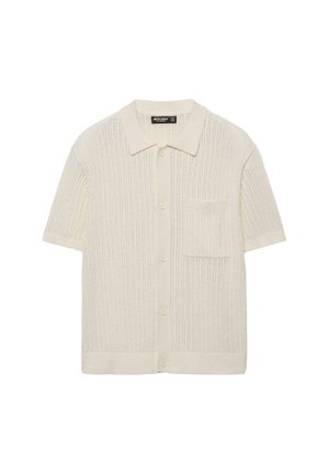 Beżowy krótki kardigan z dzianiny z kołnierzykiem, guzikami z przodu oraz jedną kieszenią na piersi.