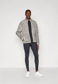 Jasnoszara kurtka na zamek z teksturowanym wykończeniem, połączona z czarną dopasowaną koszulą i czarnymi legginsami. Całość dopełniają białe trampki.