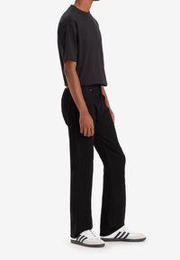 Camiseta negra de manga corta, combinada con jeans negros y zapatillas blancas con rayas negras. Diseño y ajuste sencillos y casuales.