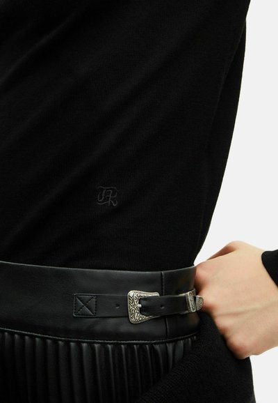 Maglione nero con texture a coste, caratterizzato da un piccolo logo ricamato. Abbinato a una ampia cintura in pelle nera, decorata con una fibbia argentata.