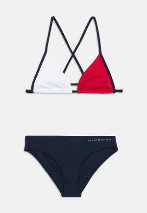 Conjunto de bikini que incluye un top de triángulo blanco y rojo con tirantes cruzados, y la parte inferior azul marino con el logo "TOMMY HILFIGER".