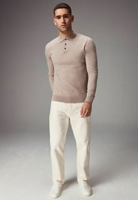 Pulover din tricot de culoare bej deschis, cu guler și o închidere cu trei nasturi, asortat cu pantaloni albi cu croială dreaptă și adidași albi.