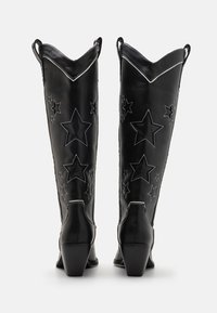 Black leather knee-high boots with star cutouts, white stitching, pointed tops, and block heels. Smooth texture with a shiny finish.