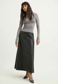 Top grigio a maniche lunghe a coste abbinato a una gonna maxi in pelle nera. L'outfit presenta una silhouette aderente e una texture elegante.