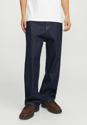 Jean en denim bleu foncé avec une coupe décontractée, ornés de surpiqûres jaunes et de poches latérales, accompagnés de chaussures à lacets marron.