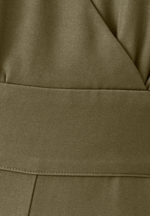 Gros plan sur un tissu vert olive avec un motif de tissage diagonal et une couture visible, probablement une partie d'un vêtement au design structuré en couches.