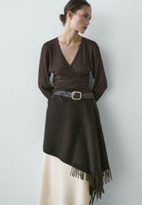 Brun omslagstop med dyb V-hals, kombineret med en nederdel med en cremefarvet sektion og frynset kant. Færdiggjort med et bredt brunt bælte.