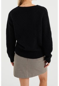 Černý pletený svetr se vzorem chevron na zádech, v kombinaci s přiléhající sukní se vzorem psi zuby. Měkká textura a jednobarevná.