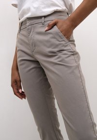 Graue, maßgeschneiderte Hose mit glatter Textur, seitlichen Taschen und schmalem Schnitt. Getragen mit einem weißen T-Shirt, das einen lässigen Look zeigt.