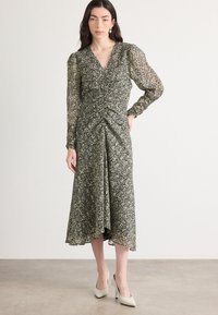 Robe midi à imprimé floral avec décolleté en V, devant plissé et manches longues bouffantes dans des tons de noir et de vert. Tissu lisse et silhouette fluide.