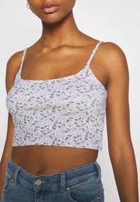 Lavendelcroppad topp med ribbad textur, prydd med ett blommönster i gult och vitt. Spaghetti-remmar och fyrkantig halsringning.