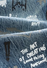Tessuto di denim con sfondo blu, testo stampato in bianco e grigio e vari accenti grafici. Il testo include frasi come "ART" e "AWESOME".
