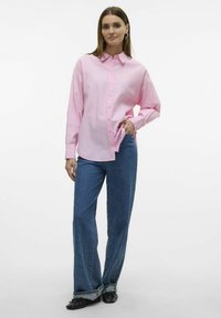 Lichtroze gestreepte button-up shirt met een ontspannen fit, gecombineerd met een wijd uitgesneden blauwe jeans en zwarte schoenen. Lange mouwen en kraagdetails zichtbaar.