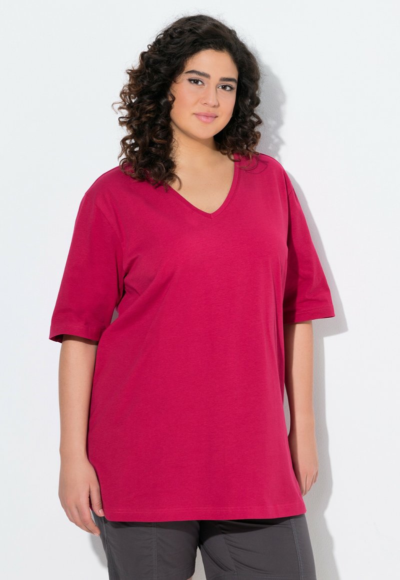 T-shirt di cotone fucsia con scollo a V e maniche corte, caratterizzato da una vestibilità morbida e una texture liscia. Indossato con pantaloni corti grigi.
