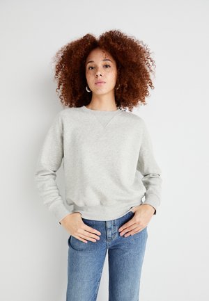 Grå hettegenser med rund hals og ribbekanter. Har en subtil tekstur, tettsittende i midjen, brukt sammen med blå høytlivsjeans.