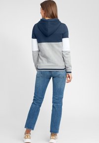 Felpa con cappuccio con la parte superiore blu navy, il centro grigio e la parte inferiore bianca. Composizione in misto cotone, orlo a costine, vestibilità comoda. Abbinata a jeans blu.