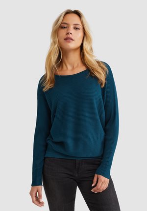 Teal geribbelde gebreide trui met een brede halslijn en zwarte jeans. Lange mouwen en een relaxte pasvorm met een gestructureerde afwerking.