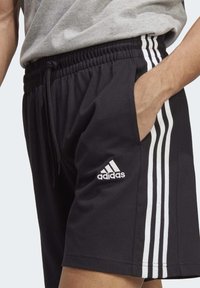 Čierne športové šortky s bielym trojprúžkom na stranách, elastický pás so šnúrkou a logom značky na nohe.