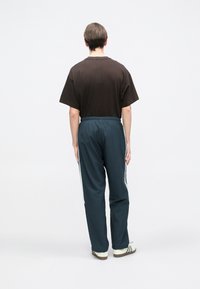 Ruda medvilnės marškinėliai trumpomis rankovėmis, derinami su tamsiai mėlynomis sportinėmis kelnėmis, kurių šonuose yra baltos juostos ir elastinga juosta liemeniui. Įtraukti kasdieniai batai.