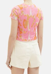Top de manga corta en color rosa con un diseño abstracto fluido en tonos naranja, amarillo y crema; combinado con pantalones cortos blancos con bolsillos traseros.