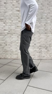 Pantaloni grigi su misura con taglio dritto, dotati di tasche laterali e una tasca posteriore. Abbinati a scarpe nere e una camicia bianca a maniche lunghe.