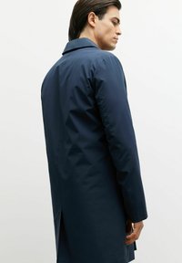 Granatowy, wodoodporny płaszcz o prostym kroju, z dużym kołnierzem i bocznymi rozcięciami dla swobody ruchów; gładka faktura, minimalistyczny design.