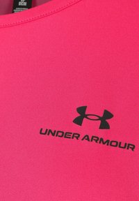 Růžové sportovní tričko vyrobené z jemné tkaniny s kulatým výstřihem, se černým logem Under Armour a textem v dolní části.