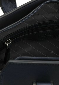Navy leren handtas interieur met een ritsvak en gestreepte stofvoering. Kenmerken zijn onder andere een gestructureerd oppervlak en contrasterende blauwe stiksels.