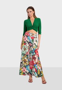 Top corto verde con maniche lunghe abbinato a una gonna maxi a fiori colorata. La gonna presenta grandi disegni di fiori vivaci.