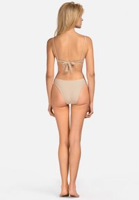 Beżowy bikini z delikatnym wiązaniem z tyłu, wysokim wycięciem na nogi i minimalnym kryciem, o gładkiej, błyszczącej fakturze.