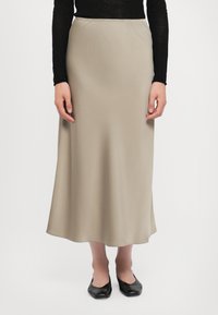 Beige sateng maxiskjørt med elastisk midjebånd, med en glatt tekstur og en flytende silhuett, parret med svarte leppesko.