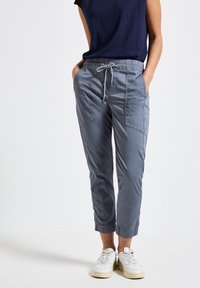 Grå elastiska midjebyxor med sidfickor, med en avsmalnande design och uppvikta anklar. Matchas med vita sneakers.