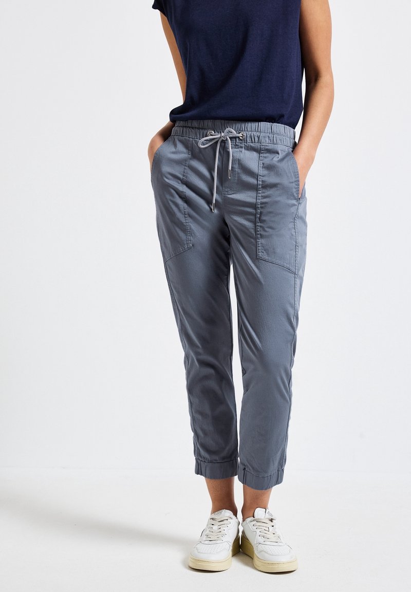 Grå elastiska midjebyxor med sidfickor, med en avsmalnande design och uppvikta anklar. Matchas med vita sneakers.