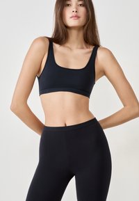 Schwarzer Sport-BH mit breiten Trägern und quadratischem Ausschnitt, kombiniert mit hochgeschnittenen schwarzen Leggings, beide aus einem glatten, dehnbaren Material hergestellt.