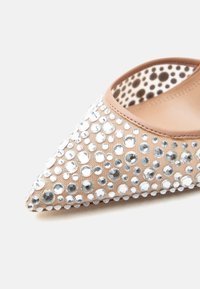 Μπεζ παπούτσι με μυτερή μύτη, διακοσμημένο με κρυστάλλινες πέτρες διάφορων μεγεθών και εσωτερική επένδυση με πουά σχέδιο.