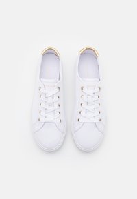 Sneaker bianchi in canvas con occhielli dorati e dettagli sul tallone, caratterizzati da una suola piatta e una punta rotonda, allacciate con lacci bianchi.